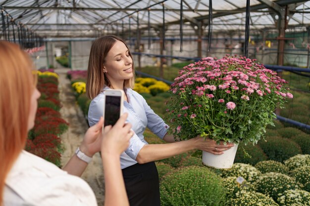 Schließen Sie herauf Frauenhände, die Telefon halten und Foto des Mädchens mit Blumen machen.