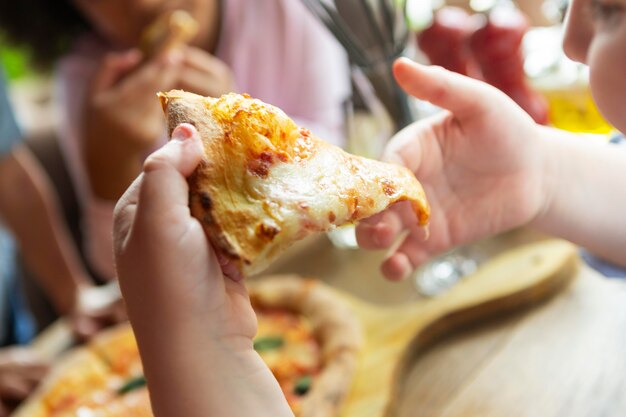 Schließen Sie herauf Kinderhände, die Pizzastück halten