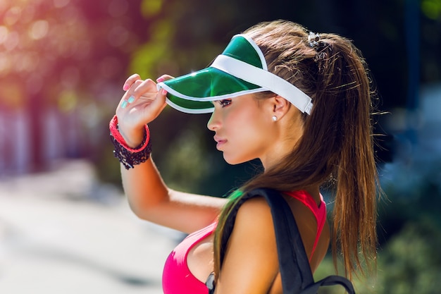 Schließen Sie herauf Lebensstilporträt der hübschen jungen Frau der Fitness in der stilvollen Kappe, die rosa Sport-BH und trägt