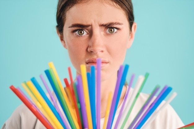 Schließen Sie herauf Mädchen mit bunten Plastikstrohhalmen, die traurig in Kamera über buntem Hintergrund schauen Hören Sie auf, Plastikstrohhalme zu verwenden