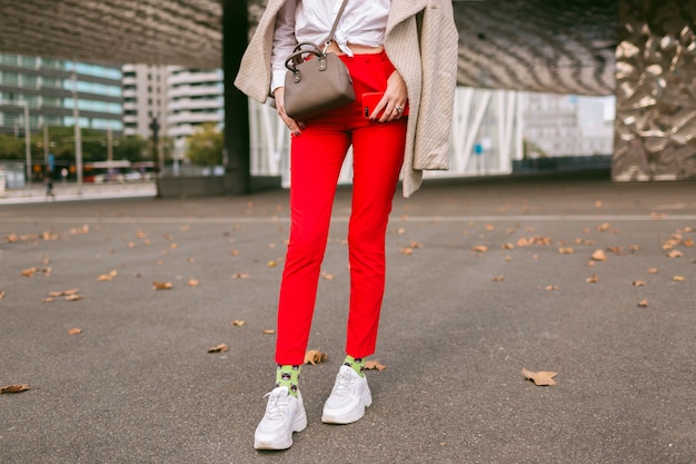 Kostenloses Foto schließen sie herauf modedetails, junge frau, die trendige rote hosen lustige socken und hässliche modeschuhe trägt, beige eleganter mantel, der auf der straße nahe geschäftszentren, herbstzeit aufwirft.