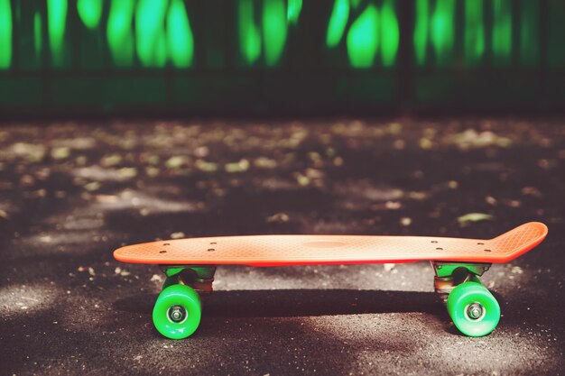 Schließen Sie herauf orange Penny Skateboard auf Asphalt hinter grüner Wand