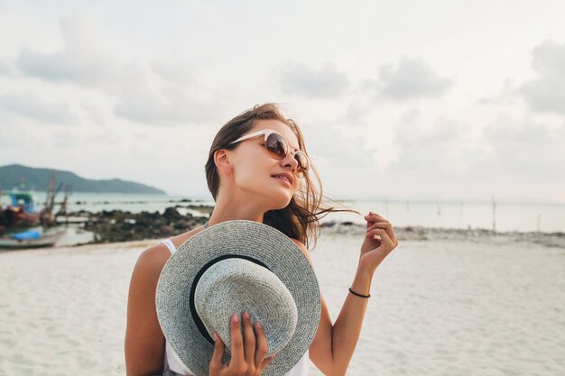 Schließen Sie herauf Porträt der jungen attraktiven lächelnden Frau, die Strohhut am tropischen Strand trägt Sonnenbrille hält