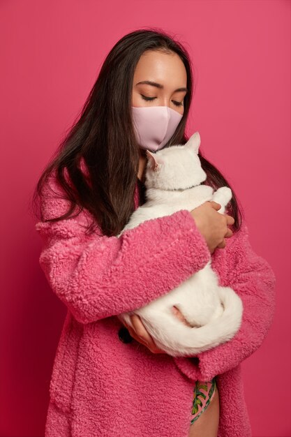 Schließen Sie herauf Porträt der jungen schönen Frau mit Schutzmaske, die eine Katze lokalisiert hält