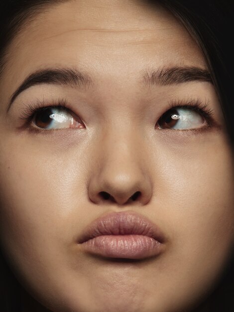 Schließen Sie herauf Porträt der jungen und emotionalen chinesischen Frau. Hochdetailliertes Fotoshot eines weiblichen Models mit gepflegter Haut und strahlendem Gesichtsausdruck. Konzept menschlicher Emotionen. Denken, zur Seite schauen.