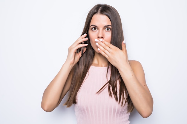 Schließen Sie herauf Porträt der schockierten Frau, die mit jemandem am Telefon auf weißer Wand spricht.