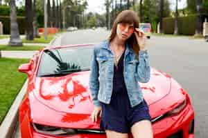 Kostenloses Foto schließen sie herauf porträt der überraschten brünetten frau, die auf der motorhaube des erstaunlichen roten cabrio-sportwagens in kalifornien sitzt.