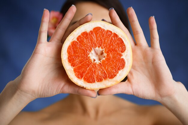 Schließen Sie herauf Porträt der zarten jungen Frau, die geschnittenes Orange über blaue Wand hält