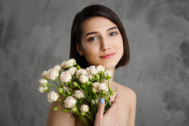 Schließen Sie herauf Porträt der zarten jungen Frau mit Blumen über graue Wand