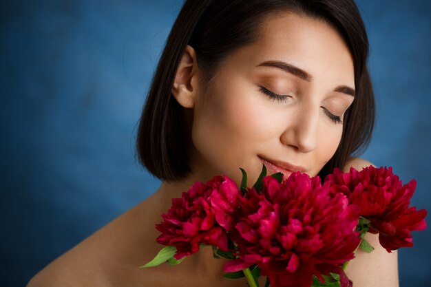 Schließen Sie herauf Porträt der zarten jungen Frau mit den roten Blumen über der blauen Wand