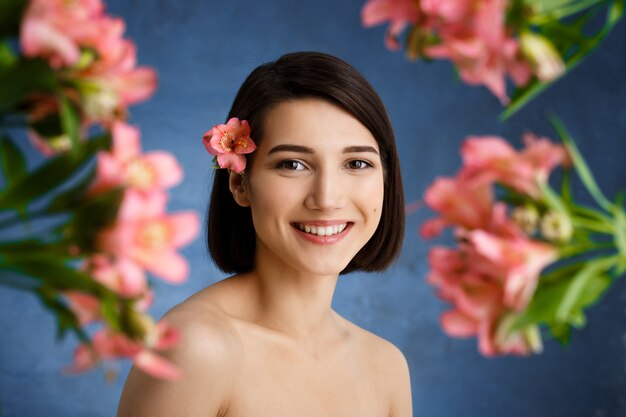 Schließen Sie herauf Porträt der zarten jungen Frau mit den verwischten rosa Blumen über der blauen Wand