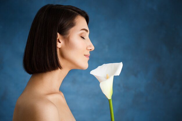 Schließen Sie herauf Porträt der zarten jungen Frau mit weißer Blume über blauer Wand