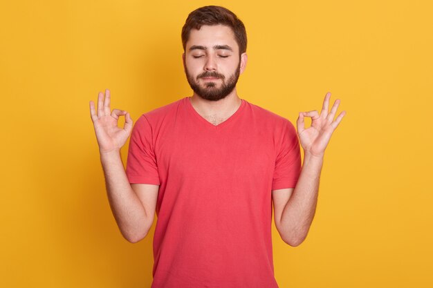 Schließen Sie herauf Porträt des attraktiven Mannes kleidet rotes lässiges T-Shirt, das ok Zeichen mit geschlossenen Augen gestikuliert