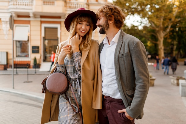 Schließen Sie herauf Porträt des erstaunlichen stilvollen Paares in der Liebe, die romantische Ferien in der europäischen Stadt verbringt. Hübsche blonde Frau im Hut und im lässigen Kleid lächelnd und auf ihrem gutaussehenden Mann mit Bart schauend.