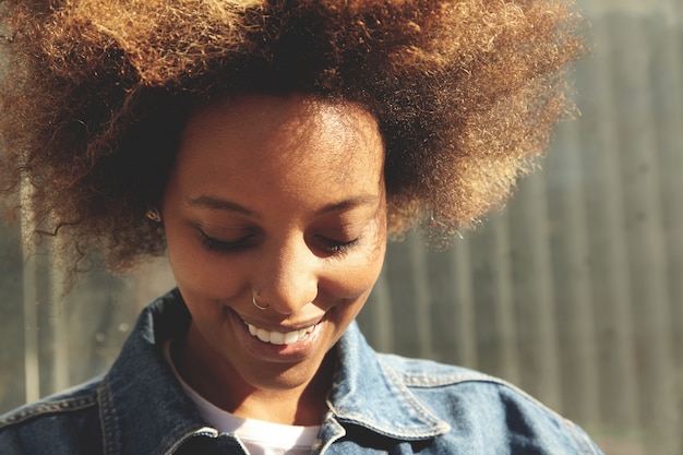 Schließen Sie herauf Porträt des glücklichen afrikanischen Studentenmädchens mit stilvollem Afro-Haarschnitt und Gesichtspiercing, das fröhlich lächelt