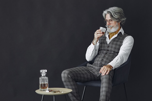 Kostenloses Foto schließen sie herauf porträt des grinsenden altmodischen mannes. gentelman sitzt auf einem stuhl. großvater mit einem glas whisky.