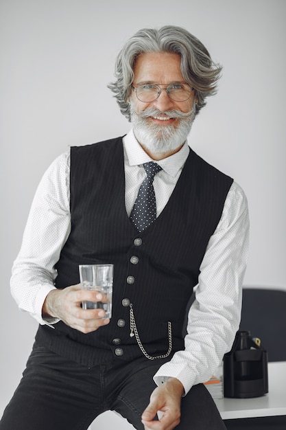 Schließen Sie herauf Porträt des grinsenden altmodischen Mannes. Großvater mit einem Glas Wasser.