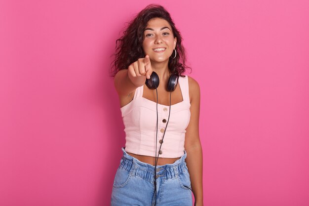 Schließen Sie herauf Porträt des hübschen Mädchens, das mit ihrem Zeigefinger zur Kamera, charmante Frau trägt Rosentop und Jeans poiting