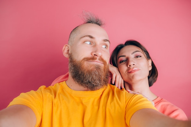 Schließen Sie herauf Porträt des jungen, kaukasischen, attraktiven, reizenden, niedlichen, süßen, lächelnden, positiven Paares im lässigen machen Selfie auf Handy auf rosa Hintergrund