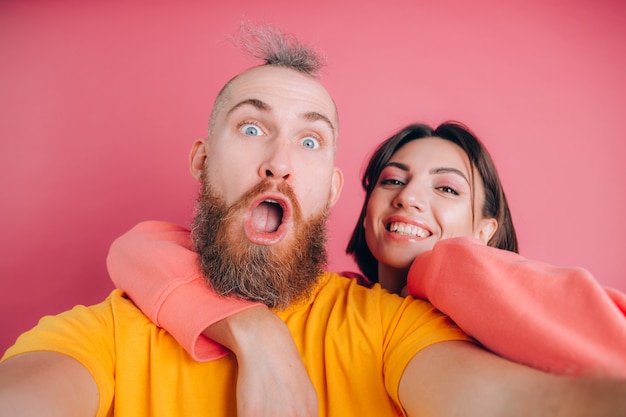 Schließen Sie herauf Porträt des jungen, kaukasischen, attraktiven, reizenden, niedlichen, süßen, lächelnden, positiven Paares im lässigen machen Selfie auf Handy auf rosa Hintergrund