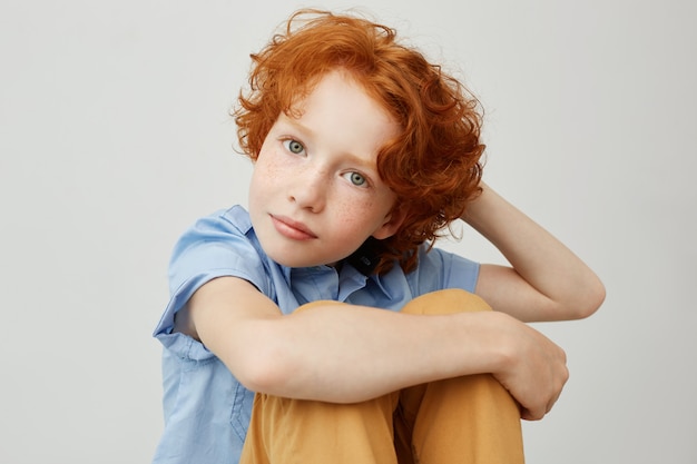 Kostenloses Foto schließen sie herauf porträt des niedlichen kleinen jungen mit dem gelockten ingwerhaar, das auf boden sitzt