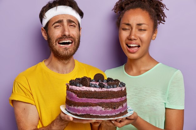 Schließen Sie herauf Porträt des traurigen aktiven Paares, das mit einem großen Kuchen aufwirft