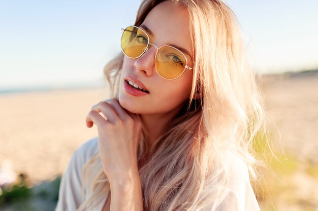 Schließen Sie herauf Porträt des verspielten lächelnden blonden Mädchens, das mit Haaren spielt, Spaß hat und Sommer am Strand genießt.