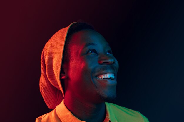 Schließen Sie herauf Porträt eines glücklichen jungen Afroamerikanermannes, der gegen schwarzen Neonstudiohintergrund lächelt
