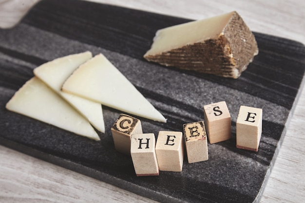 Schließen Sie herauf Seite fokussierte Buchstaben Käse voraus unkonzentrierten Ziegenkäse auf Marmorsteinbrett isoliert auf hölzernen leeren Tisch