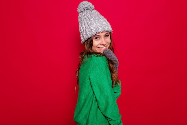 Schließen Sie herauf Studio-Porträt der glücklichen entzückenden jungen Dame, die graue Wintermütze und grünen Pullover aufwirft und lächelt