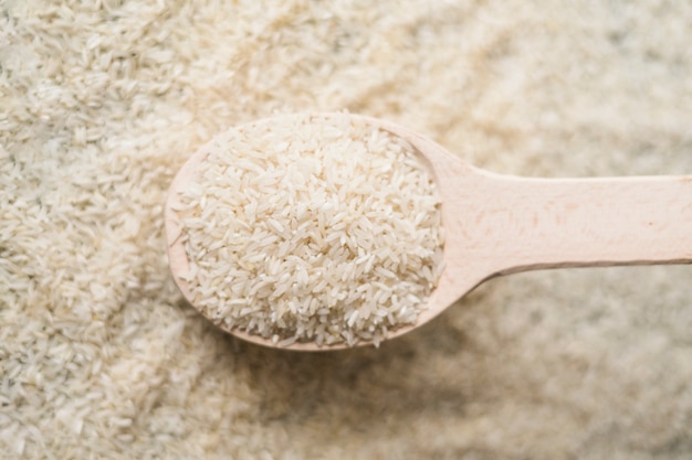 Schließen Sie herauf ungekochten Reis im hölzernen Löffel auf Reishintergrund