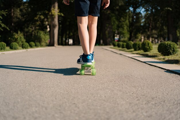 Schließen Sie oben Beine in blauen Turnschuhen, die auf grünem Skateboard in Bewegung reiten. Aktiver urbaner Lebensstil der Jugend, Ausbildung, Hobby, Aktivität. Aktiver Outdoor-Sport für Kinder. Skateboarding für Kinder.