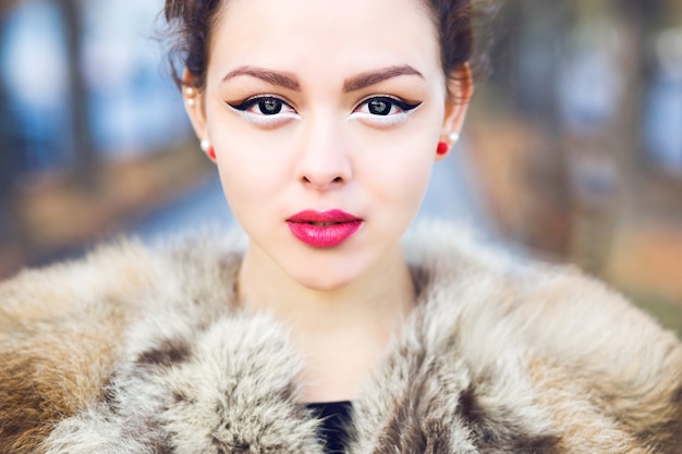 Schließen Sie oben im Freien Modeporträt des schönen asiatischen Mädchens mit der perfekten Haut, die Pelzjacke, das helle Make-up der Nadel oben und die Augenlinsen trägt. Herbstporträt im Freien.