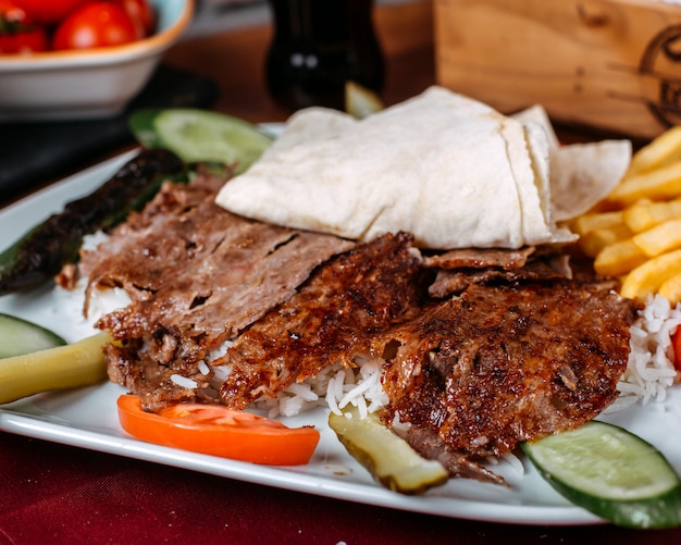 Schließen Sie oben vom türkischen Kebabfleisch mit Reispommes und frischem Gemüse auf einem Teller