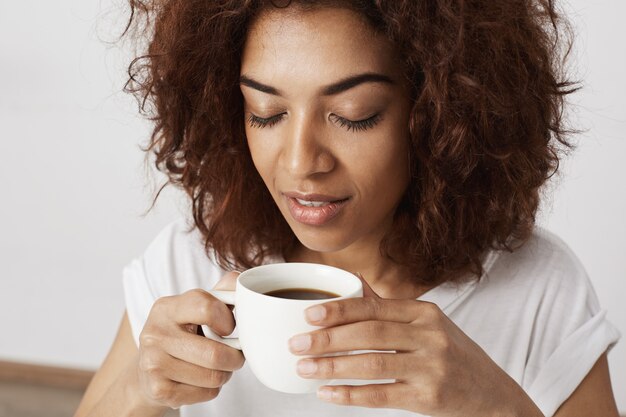 Schließen Sie oben von afrikanischem Mädchen, das Tasse riechenden Kaffee mit geschlossenen Augen hält.