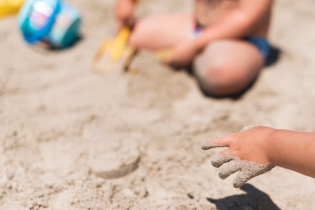 Schließen Sie oben von den Kinderhänden, die mit Sand am Strand spielen