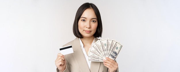 Schließen sie oben von der asiatischen geschäftsfrau-bürodame, die kreditkarte und gelddollar zeigt, die im anzug über weißem hintergrund stehen