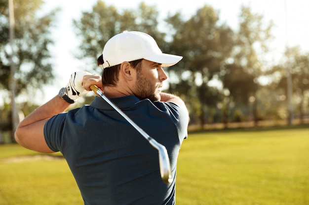 Schließen Sie oben von einem jungen konzentrierten Mann, der Golfball schießt