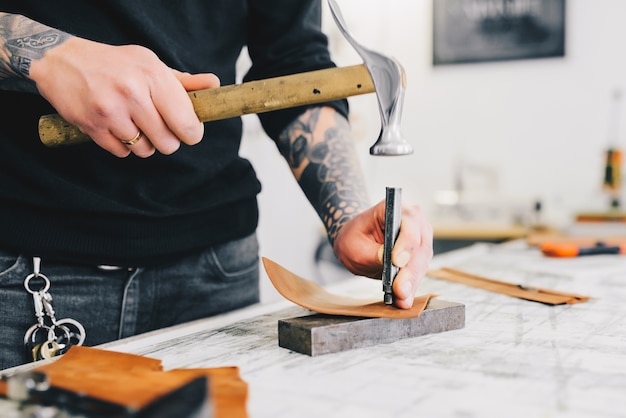 Schließen Sie oben von einem ledernen Handwerker, der mit Leder unter Verwendung des Hammers arbeitet.