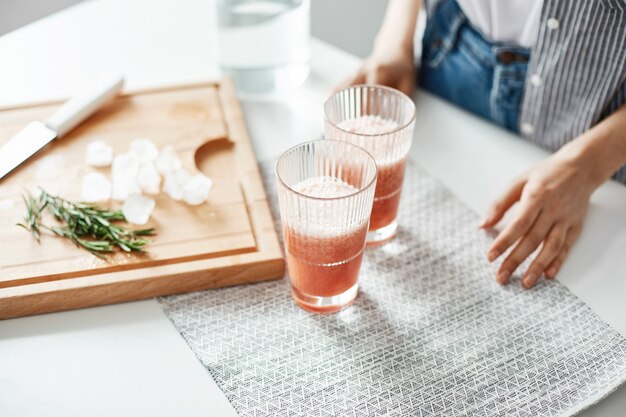 Schließen Sie oben von Frauenhandgläsern mit Grapefruit-Detox-Diät-Smoothie-Rosmarin und Eisstücken auf Holzschreibtisch.