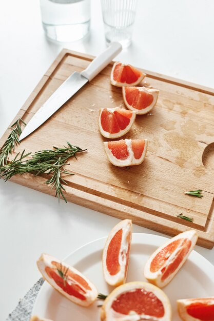 Schließen Sie oben von Grapefruitstücken Messer und Rosmarin auf Holzschreibtisch. Speicherplatz kopieren.