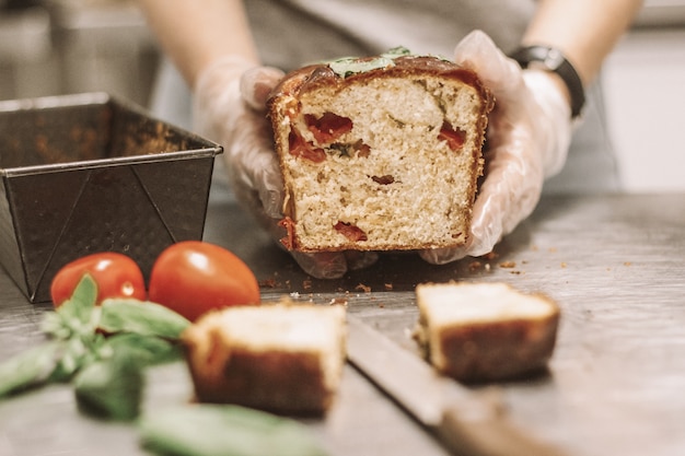 Schließen Sie Schuss von Chef, der einen Laib Brot nahe Tomaten mit einem unscharfen Hintergrund hält