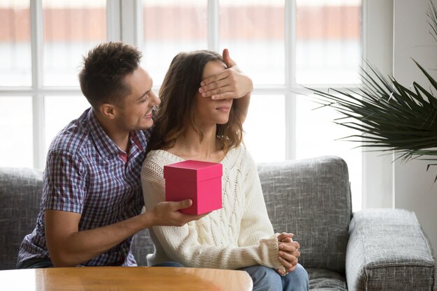 Schließende Augen des liebevollen Ehemanns der Frau, die romantisches Überraschungsgeschenk darstellt