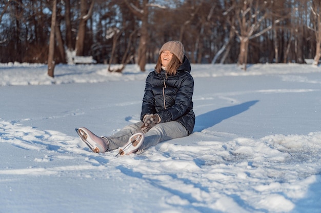 Schlittschuhe, Junge Frau lernt Schlittschuhlaufen, fällt, sitzt auf dem Schnee, Wintersport, Schnee, Winterspaß.