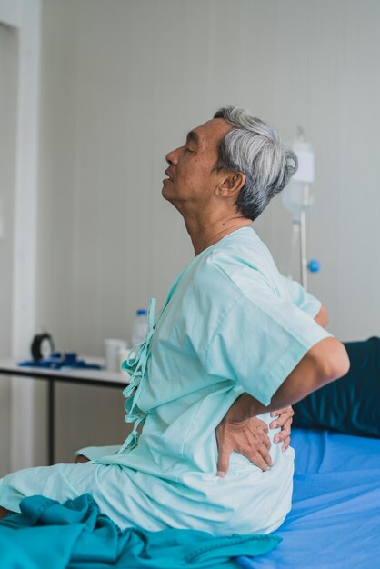 Schmerzen und rückenschmerzen alter senior asiatischer großvater in patientenuniform leiden unter körperproblemen gesundheitsideenkonzept