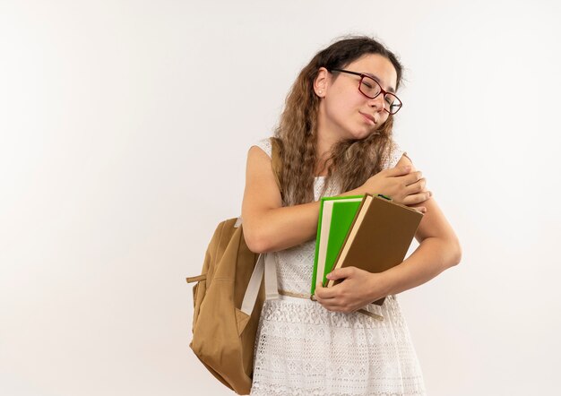 Schmerzendes junges hübsches Schulmädchen, das Brille und Rückentasche hält Bücher hält, die Hand auf Arm mit geschlossenen Augen setzen, lokalisiert auf Weiß mit Kopienraum