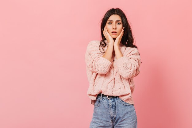 Schnappschuss eines dolorösen dunkelhaarigen Mädchens im rosa Studio. Frau im Strickpullover schaut traurig in die Kamera.