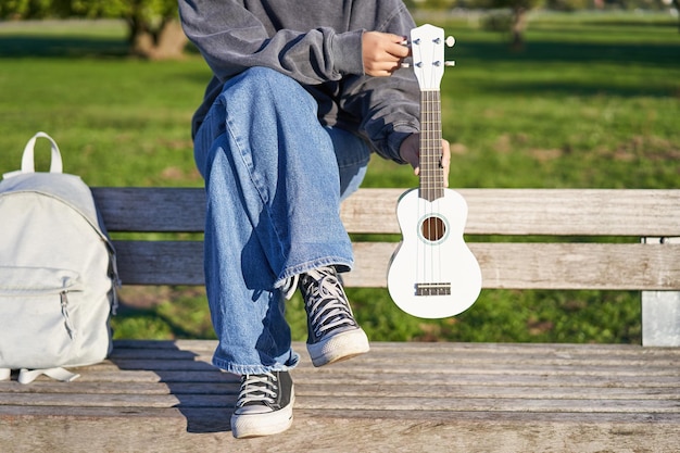 Kostenloses Foto schnappschuss eines jungen mädchens in turnschuhen und jeanshänden, die ein ukulele-musikinstrument halten, während sie