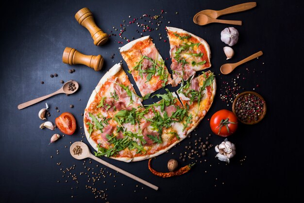 Schneidet italienische Pizza mit Geräten und Bestandteilen über schwarzer Küche worktop