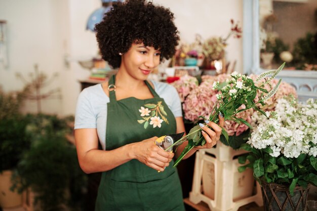 Schnittstange der jungen Frau von Blumen mit Baumschere im Blumenladen